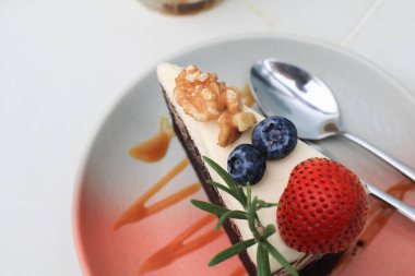 Seramik tabakta koyu bira keki ve çilek, yabanmersini, biberiye ve fıstık ile süslenmiş..