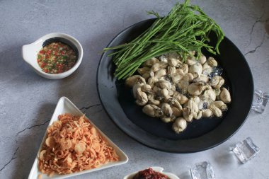 Deniz ürünleri soslu taze istiridye, kızarmış kırmızı soğan ve siyah tabakta buzlu Acacia yaprakları. Sağlıklı deniz ürünleri