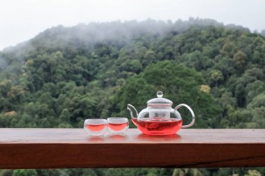 Bardakta sıcak çay ve sabah sisli dağ manzaralı demlik. Aroma içeceği doğada var.