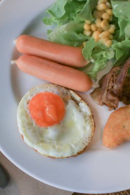 Amerikan kahvaltısı, sebze salatası, sosis ve beyaz tabakta yumurta. Sabahları sağlıklı besleniyorlar..