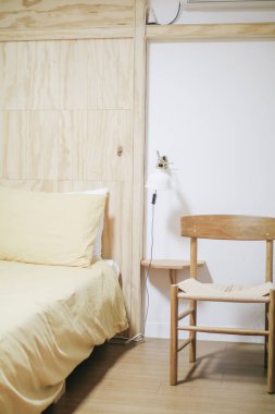 Yatak odasının içinde krem yastıklı ahşap duvarlı bir yatak. Doğal ışık. En düşük tasarım.