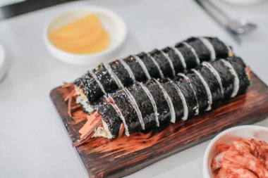 Domuz etli, sebzeli kimbub, ahşap tabakta deniz yosunlu sosis. Sarı turp ve kimçi turşusuyla yemek. Kore geleneksel yemekleri