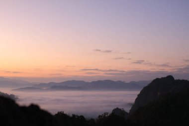Güzel sabah dağları ve güneşin doğuşuyla sisli. Barışçıl ve atmosferik bir ortam yaratıyor. Güneş doğmadan önce.