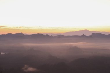 Güzel sabah dağları ve güneşin doğuşuyla sisli. Barışçıl ve atmosferik bir ortam yaratıyor. Güneş doğmadan önce.