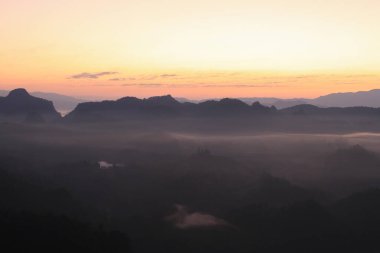 Güzel sabah dağları ve güneşin doğuşuyla sisli. Barışçıl ve atmosferik bir ortam yaratıyor. Güneş doğmadan önce.