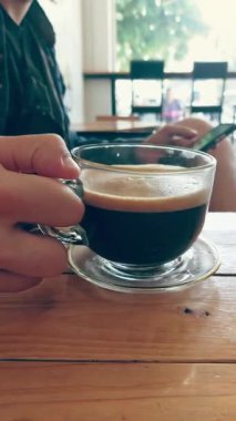 Akıllı telefon kafe 'sinde gezinirken sade kahveden bir yudum alan kişi...