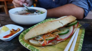 Taze banh mi sandviçin yanında erişte çorbası içen adam.