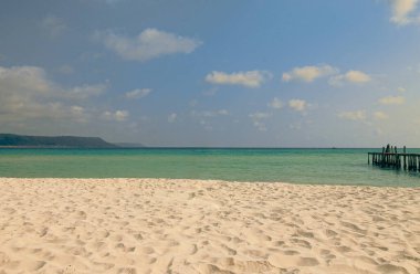 Güneşli kumsal, turkuaz okyanus dalgalarıyla buluşuyor.