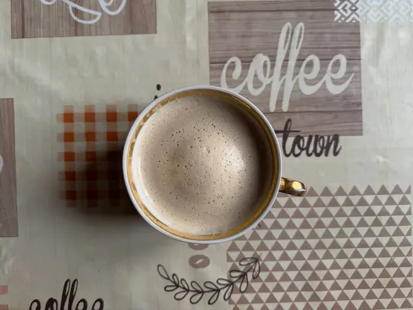 Mutfak masasında beyaz bardakta sütlü kahve ve kahve sözcüğünün olduğu masa örtüsü, üst manzara. Yüksek kalite fotoğraf