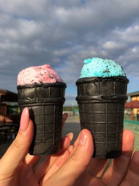 Yaz tatilinde bulanık bir şehrin arka planına sahip siyah bir külahta pembe ve mavi bir dondurma. Yüksek kalite fotoğraf