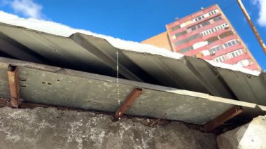 Garajın çatısındaki sıcak güneşten eriyen bir buz sarkıtı, temiz su gibi asfalta, bir evin ve mavi gökyüzünün arka planına doğru akar. Yüksek kalite 4k görüntü