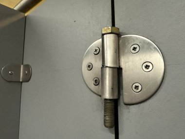 Metal silver hinge on a grey door with 6 screws screwed into the door. High quality photo