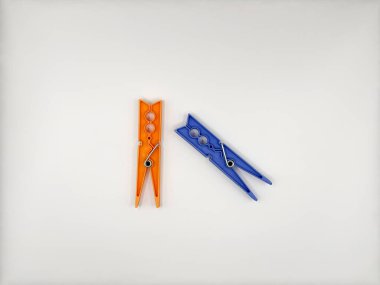 Merkezde beyaz bir zemin üzerinde mavi ve turuncu renkli metal yaylarla farklı renklerde plastik mandallar, üst görünüm. Yüksek kalite fotoğraf