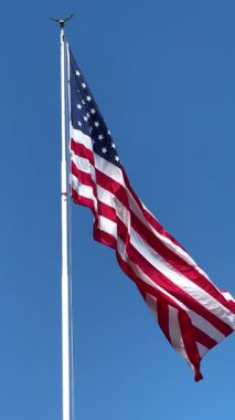 Yıldızları ve çizgileri rüzgarda dalgalanan dev bir Amerikan bayrağı, güneşli bir günde, dikey bir videoda ABD 'nin mavi gökyüzüne karşı olan gücünü yavaş çekimde gösteriyor. Yüksek kaliteli FullHD görüntüler