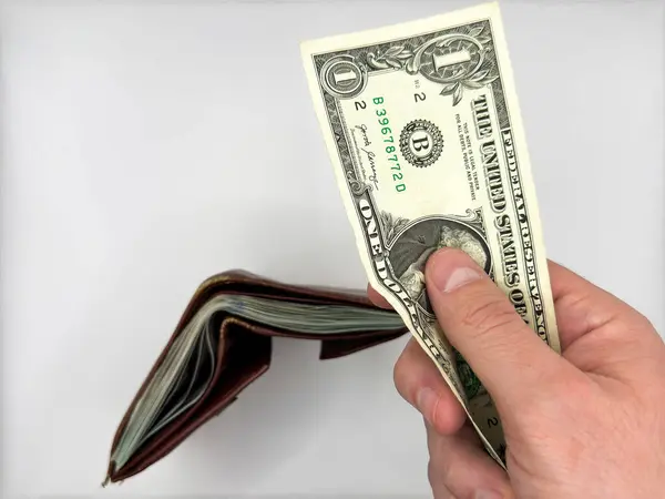 Beyaz erkek, arka plandaki eski kahverengi deri cüzdandan vergi ödemek için bir dolarlık banknot tutuyor. Yüksek kalite fotoğraf