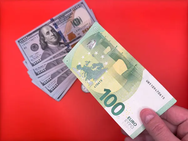 Bir adamın elinde 100 avroluk bir banknot var ve arka planda parlak kırmızı arka planda yan yana duran 100 'lük banknotlar var. Yüksek kalite fotoğraf