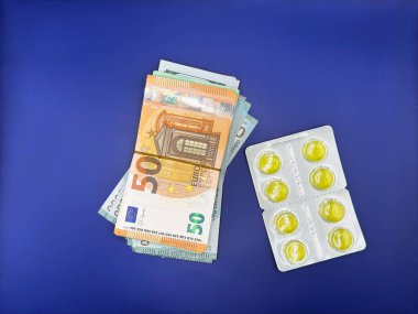 Yeni gümüş ambalajlı parlak sarı haplar. Avro ve dolar parasının yanında. Görüntünün merkezindeki parlak mavi arka planda. Yüksek kalite fotoğraf