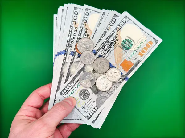 Parlak yeşil arka plan manzarasında 100 dolarlık banknotlar ve Amerikan sentleri tutan bir erkek. Yüksek kalite fotoğraf