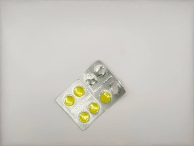 Gümüş ambalajlı açık sarı yuvarlak tabletlerden biri beyaz arka plan görünümünde. Yüksek kalite fotoğraf