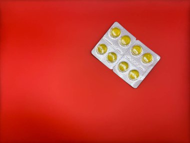 Yeni gümüş ambalajlı parlak sarı tabletler sağ tarafta parlak kırmızı arka plan, yatay olarak düzenlenmiş, üst görüş. Yüksek kalite fotoğraf