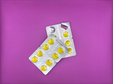 Yeni gümüş bir pakette parlak sarı tabletler ve görüntünün merkezinde parlak mor bir zemin üzerinde zaten kullanılmış bir paket dikey olarak yer almaktadır. Yüksek kalite fotoğraf