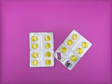 Yeni gümüş bir pakette parlak sarı tabletler ve görüntünün merkezinde parlak mor bir zemin üzerinde virüsün tedavisi için zaten kullanılmış bir paket dikey olarak yerleştirilmiş iki paket var.