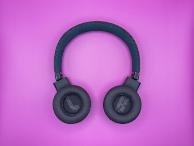 Tam boy kulaklıklar, büyük, yeşil plastikten, yumuşak kulaklıklar dışa çevrilmiş, sol ve sağ kulaklıklar gösterilmiş, ve yumuşak bir yay pembe bir resmin ortasında duruyor.