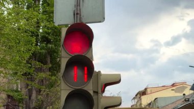 Trafik ışığı saniyeler içinde kırmızı ışığı ve geri sayımı gösteriyor. Arka planda ağaçlar ve şehir var. Yüksek kalite 4k görüntü