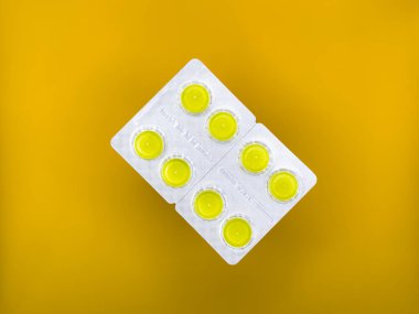 Sarı tabletler gümüş ambalajlı, sarı arka planda, görüntünün ortasında, en üstte. Yüksek kalite fotoğraf