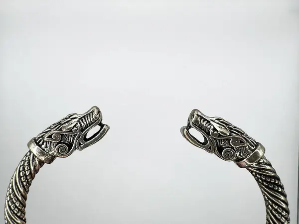 Kenarlarında iki canavar kafası olan gümüş metal Viking bileziği ve beyaz arka planda spiral şekilli ana parçası, üst manzara, nesne görüntünün merkezinde yer alıyor. Yüksek kalite fotoğraf