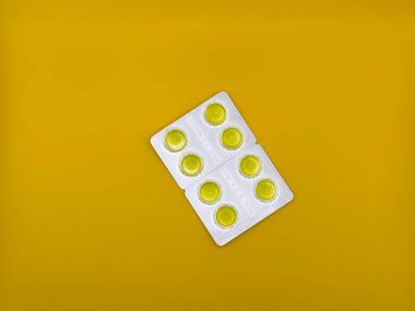 Sarı öksürük tabletleri gümüş ambalajlı, sarı arka planda, görüntünün ortasında, üst görünümde. Yüksek kalite fotoğraf