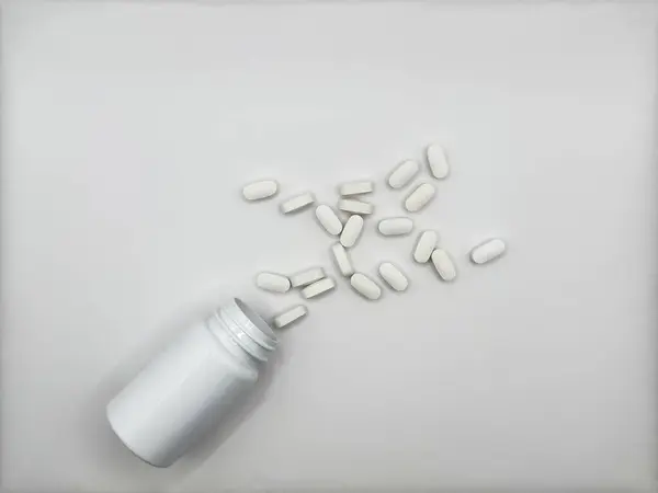 Hastalık için kullanılan beyaz haplar beyaz bir ilaç kavanozundan beyaz beyaz bir yüzeye dökülmüş vaziyette bulunurlar. Kavanoz görüntünün merkezindedir. Yüksek kalite fotoğraf