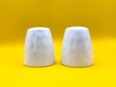 Görüntünün ortasında sarı bir zemin üzerinde iki beyaz seramik tuz ve karabiber karıştırıcı, üst manzara. Yüksek kalite fotoğraf