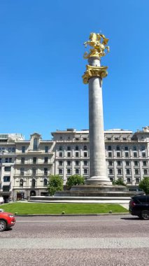 Tiflis, Gürcistan - 09 Mayıs 2025: St. George Anıtı, Tiflis Şehir Meclisi önünde diğer mimari ve arabalarla birlikte Özgürlük Meydanı 'ndaki mavi gökyüzü altında dikey video