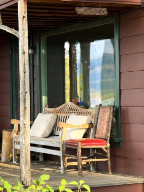 Göl kıyısındaki evin yanında boş sandalye ve bank, verandada geniş bir pencere var.!