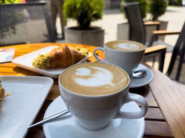 Tahta bir masanın üzerinde bir tabak kruvasanla birlikte beyaz kahve bardağı kapuçino. Kafede kahvaltı, Paris sabahı, Avrupa sabahı. Yüksek kalite fotoğraf