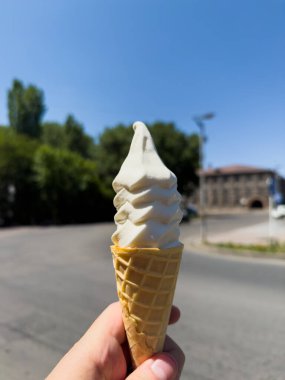 Elinde dondurma külahı tutan biri. Koni beyaz ve sarı uçlu.