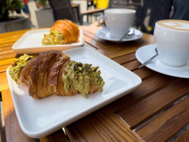 Tahta bir masanın üzerinde bir tabak kruvasanla birlikte beyaz kahve bardağı kapuçino. Kafede kahvaltı, Paris sabahı, Avrupa sabahı. Yüksek kalite fotoğraf