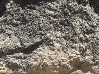 Taştan yapılmış bir duvar. Duvar gri ve birkaç çatlağı var. Duvarda küçük delikler var.