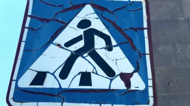 Çatlak boyalı eski yaya geçidi. Üzerinde yürüyen birinin olduğu bir tabela bozulur. İşaret mavi ve beyaz.