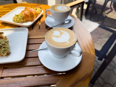Tahta bir masanın üzerinde bir tabak kruvasanla birlikte beyaz kahve bardağı kapuçino. Kafede kahvaltı, Paris sabahı, Avrupa sabahı. Yüksek kalite fotoğraf