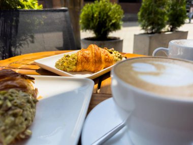 Tahta bir masanın üzerinde bir tabak kruvasanla birlikte beyaz kahve bardağı kapuçino. Kafede kahvaltı, Paris sabahı, Avrupa sabahı. Yüksek kalite fotoğraf