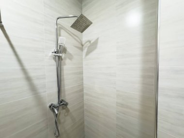 Metal saplı bir duş başlığı. Kapı kolu gümüş. Duş başlığı metal bir boruya bağlı.