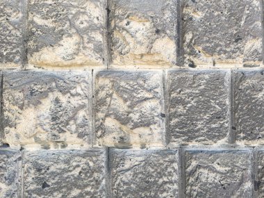 Taş ve çimentodan yapılmış bir duvar. Duvar gri ve birkaç çatlağı var. Duvarda küçük delikler var.