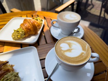 Tahta bir masanın üzerinde bir tabak kruvasanla birlikte beyaz kahve bardağı kapuçino. Kafede kahvaltı, Paris sabahı, Avrupa sabahı. Yüksek kalite fotoğraf