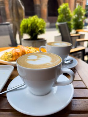 Tahta bir masanın üzerinde bir tabak kruvasanla birlikte beyaz kahve bardağı kapuçino. Kafede kahvaltı, Paris sabahı, Avrupa sabahı. Yüksek kalite fotoğraf