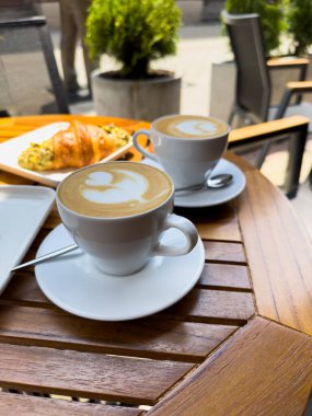 Tahta bir masanın üzerinde bir tabak kruvasanla birlikte beyaz kahve bardağı kapuçino. Kafede kahvaltı, Paris sabahı, Avrupa sabahı. Yüksek kalite fotoğraf
