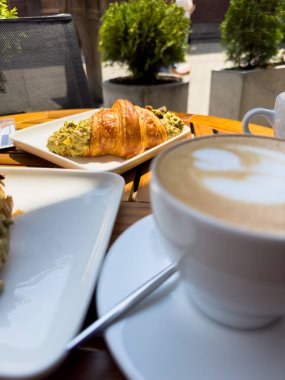 Tahta bir masanın üzerinde bir tabak kruvasanla birlikte beyaz kahve bardağı kapuçino. Kafede kahvaltı, Paris sabahı, Avrupa sabahı. Yüksek kalite fotoğraf