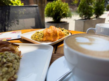 Tahta bir masanın üzerinde bir tabak kruvasanla birlikte beyaz kahve bardağı kapuçino. Kafede kahvaltı, Paris sabahı, Avrupa sabahı. Yüksek kalite fotoğraf
