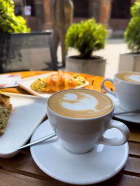 Tahta bir masanın üzerinde bir tabak kruvasanla birlikte beyaz kahve bardağı kapuçino. Kafede kahvaltı, Paris sabahı, Avrupa sabahı. Yüksek kalite fotoğraf